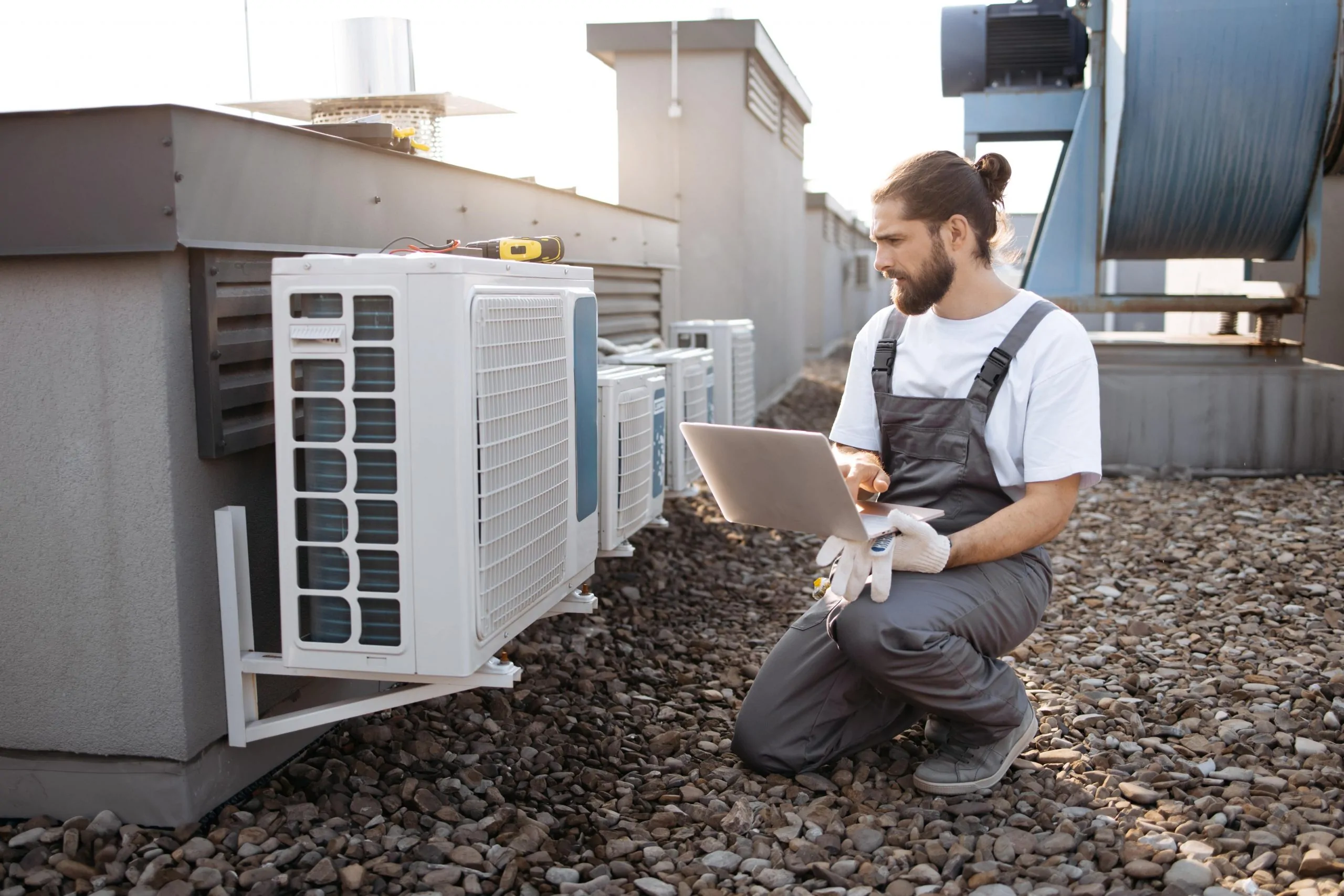 Technicien effectuant l'entretien d'unités de climatisation sur un toit avec un ordinateur portable